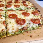 Broccoli crust pizza with melted cheese and pepperoni slices on parchment paper