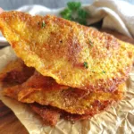 Crispy chicken chips stacked on parchment paper with golden seasoning