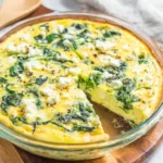 Crustless quiche feta spinach in a glass baking dish with visible spinach leaves and feta crumbles
