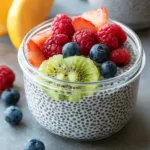 Glass jar of chia seed pudding topped with kiwi, raspberries, blueberries, and strawberries.