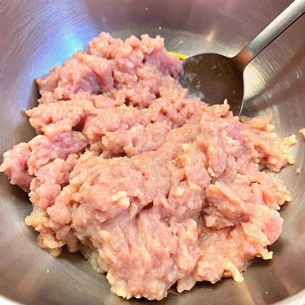 Fresh ground chicken in a stainless steel mixing bowl with a spoon